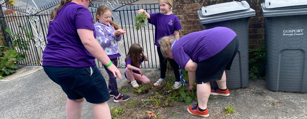 Squirrel and Beaver Scouts help their leaders pick up piles of pulled weeds