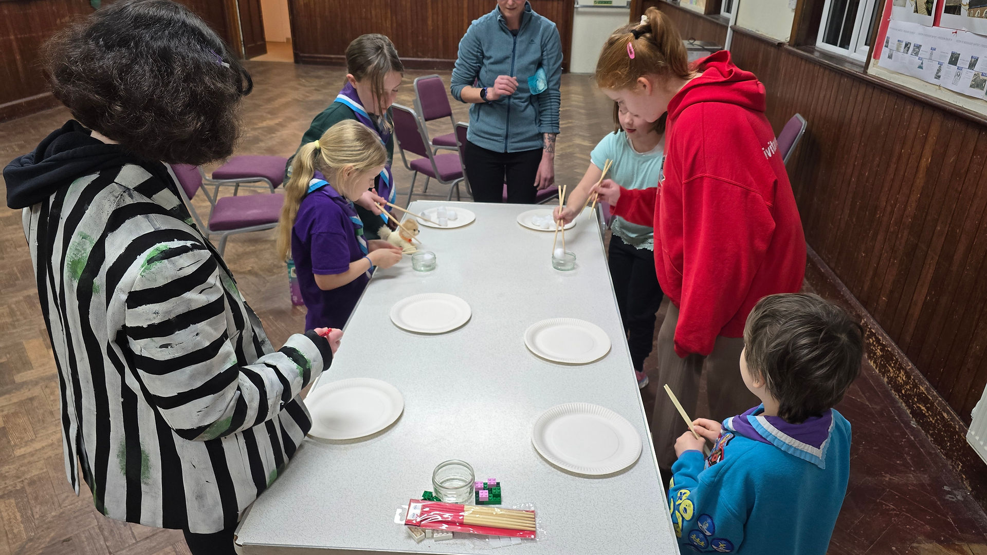 Cub Scouts and volunteers use chopsticks to move cotton balls between paper plates and small glass jars