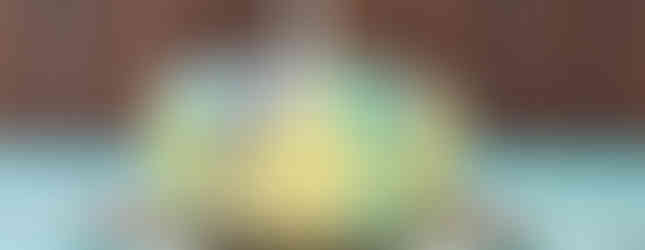 A white cake with drippy blue and purple icing sits on a table with Hey Duggee tablecloth. The cake has a "1" shaped candle lit on top of it