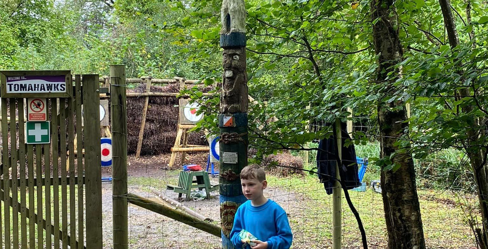A Beaver Scout stands at the bottom of a totem pole in a wooded area