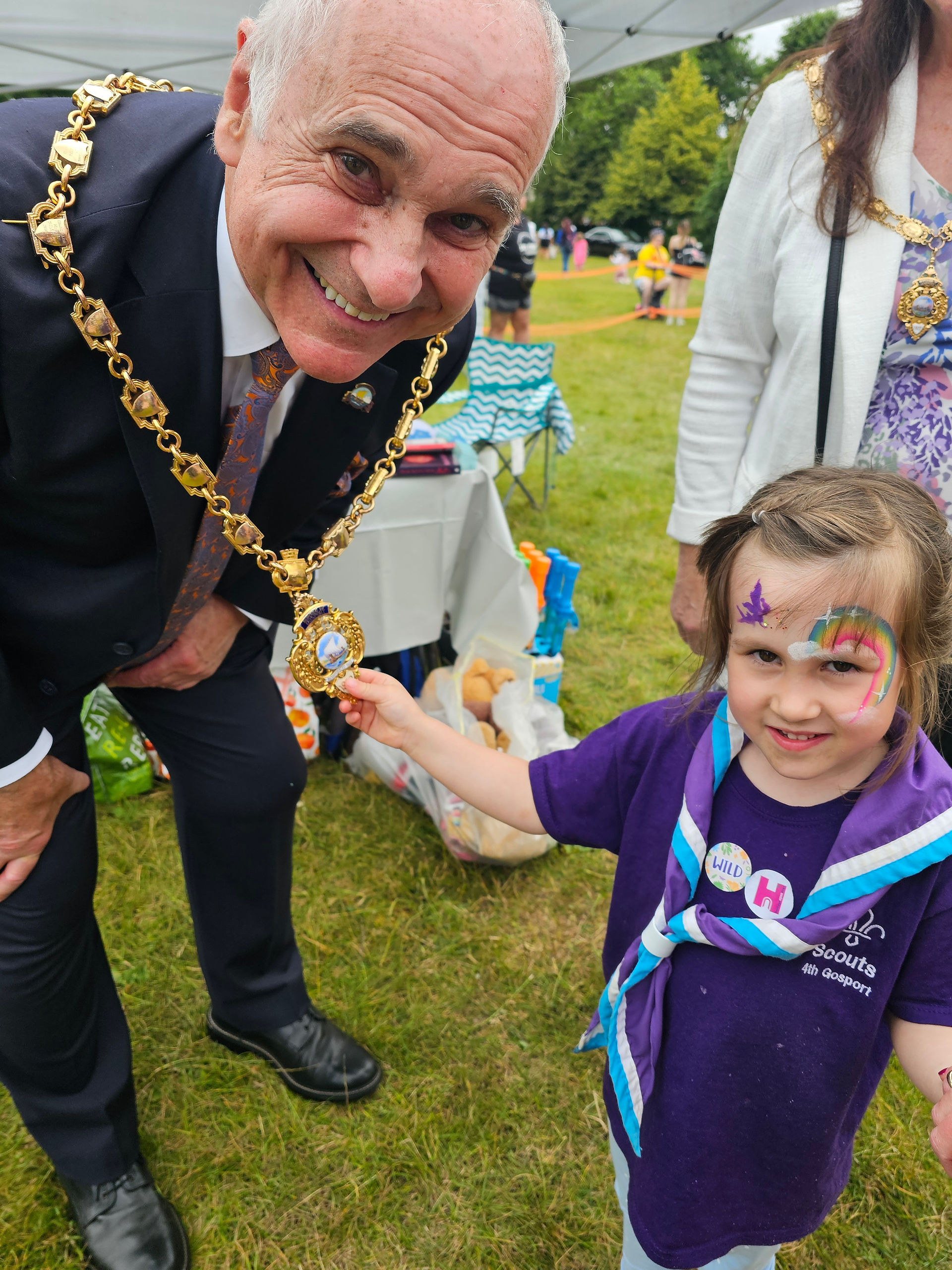 A Squirrel Scout with a face paint rainbow stands next to the Mayor of Gosport, pointing out the crest at the end of the mayoral chain