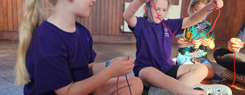 Three Beaver Scouts use lengths of paracord to practice tying knots