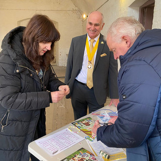 Three adults stand at a table which has sheets explaining the Morse code alphabet as well as straws and string