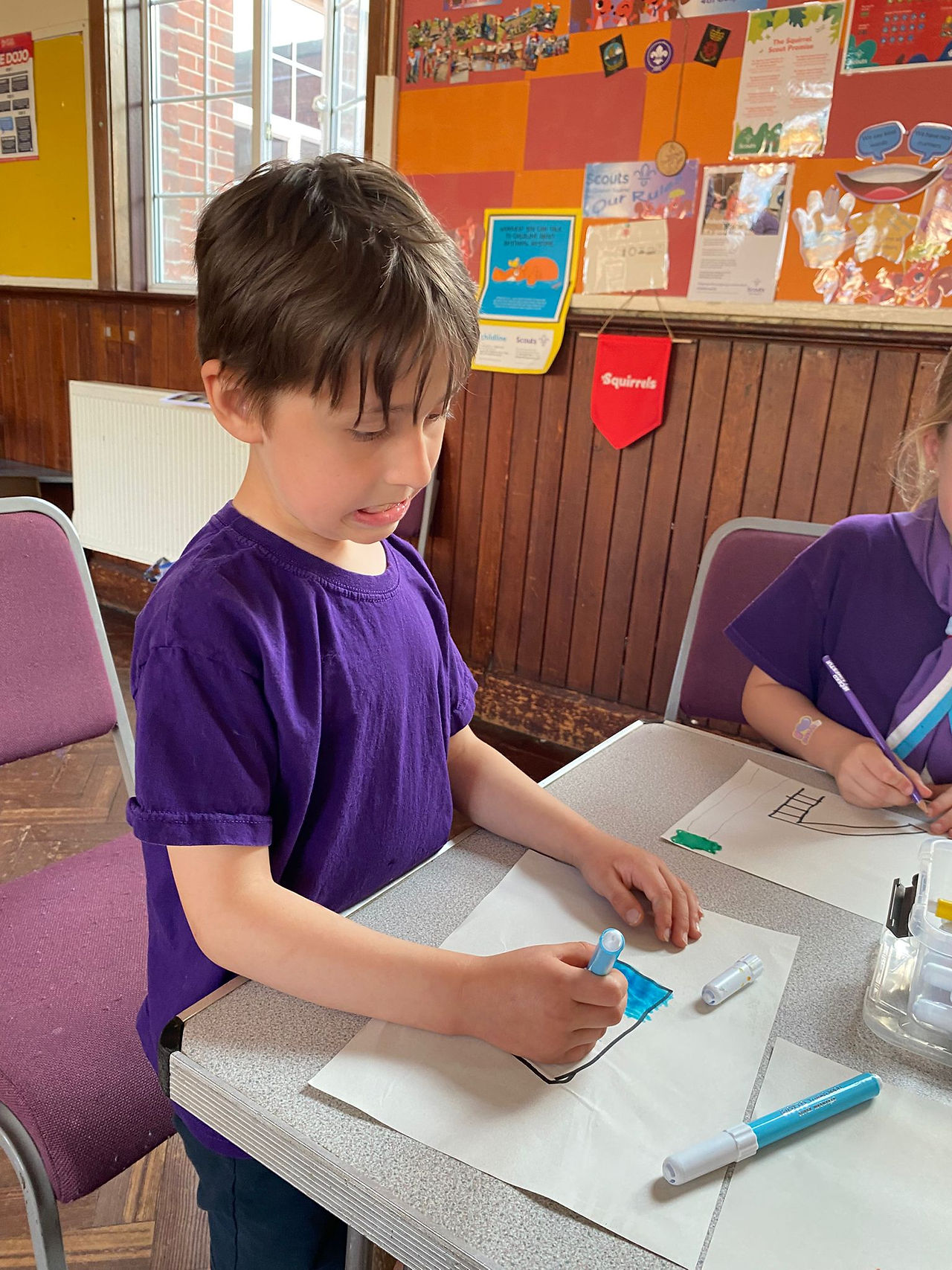 A Cub Scout uses felt tipped pens to draw on paper