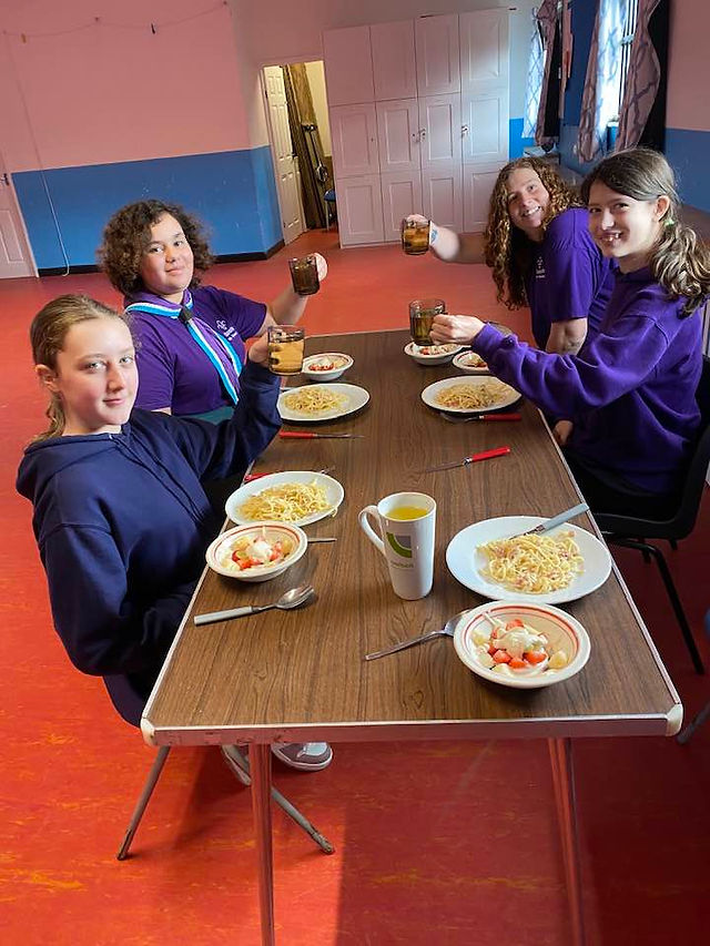 Three Scouts and their leader sit at a table with plates of food