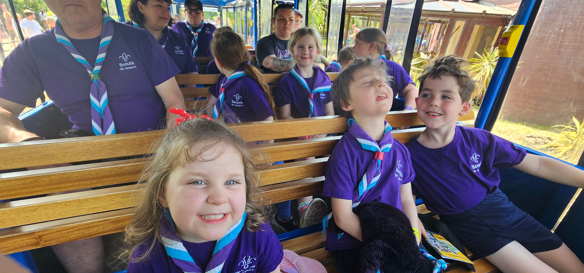 Squirrel and Beaver Scouts sit with their leaders on benches inside a road train