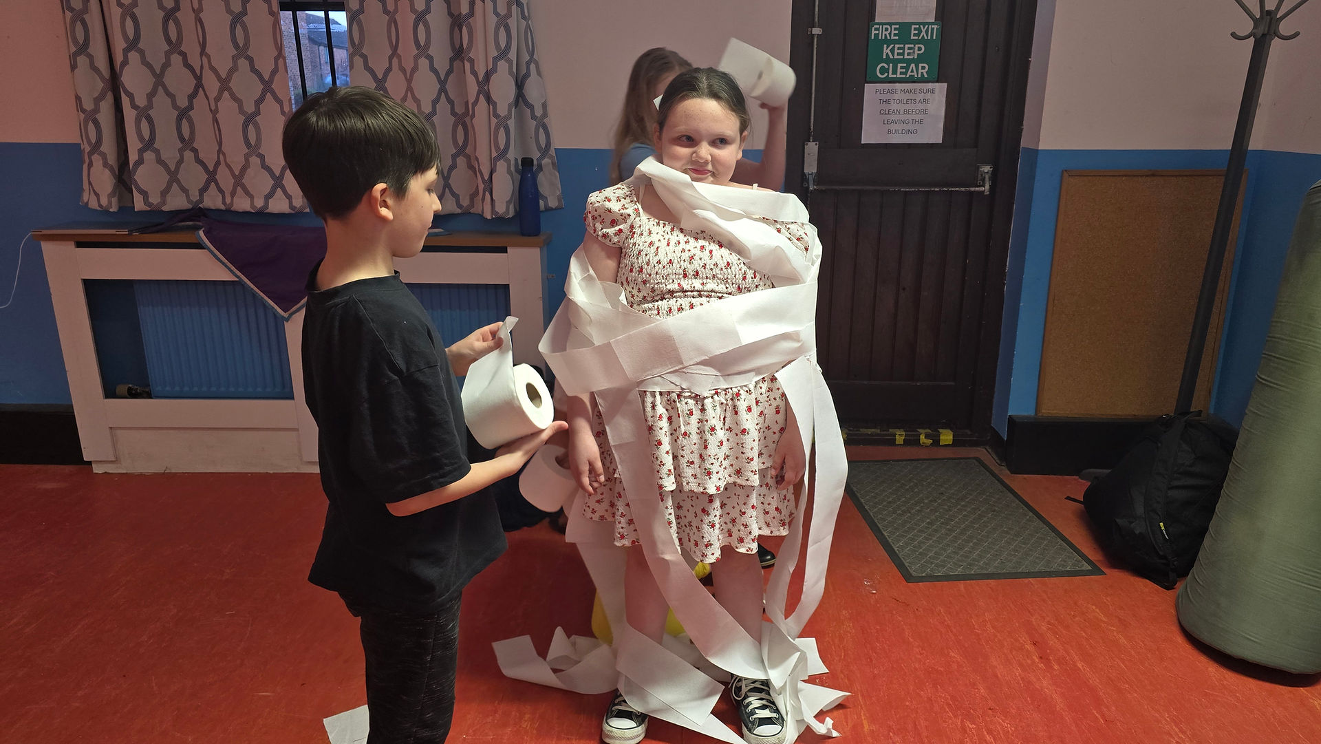 Cubs and a Scout work together to wrap another Scout in toilet paper as part of a game
