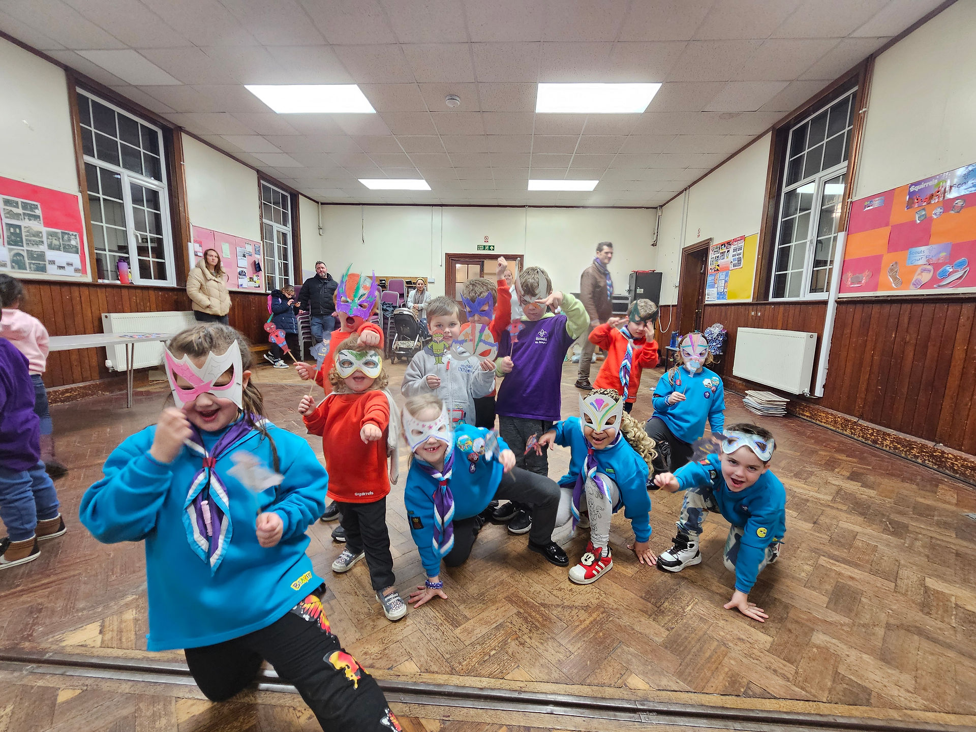 Squirrel and Beaver Scouts hold paper eye masks over their face and pose in various typical superhero poses