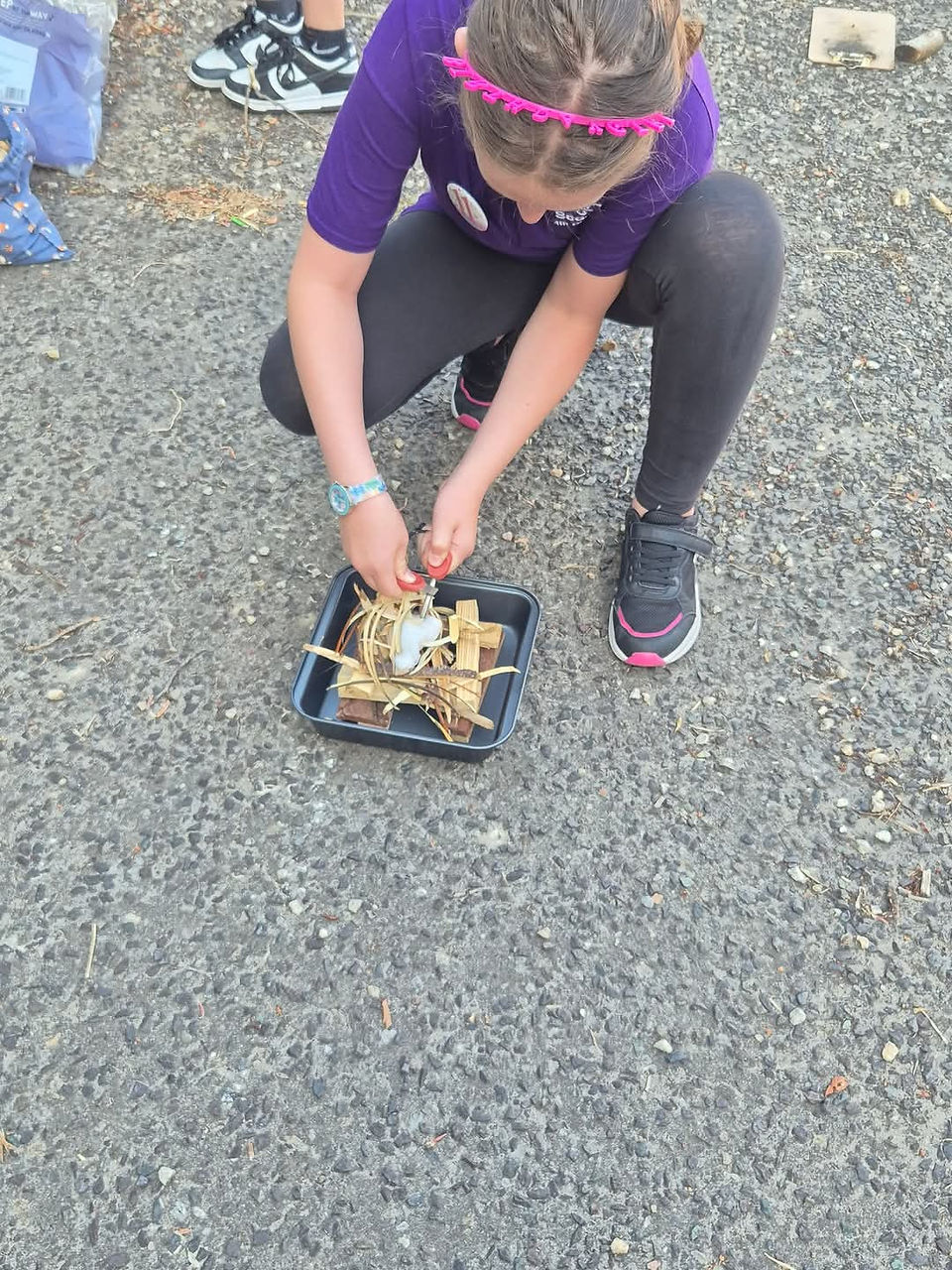 A Cub Scout uses flint and steel to light a small fire in a metal pan
