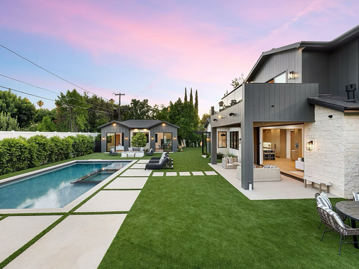 Modern backyard with rectangular pool, patio seating, and gray house under pink sunset sky.
