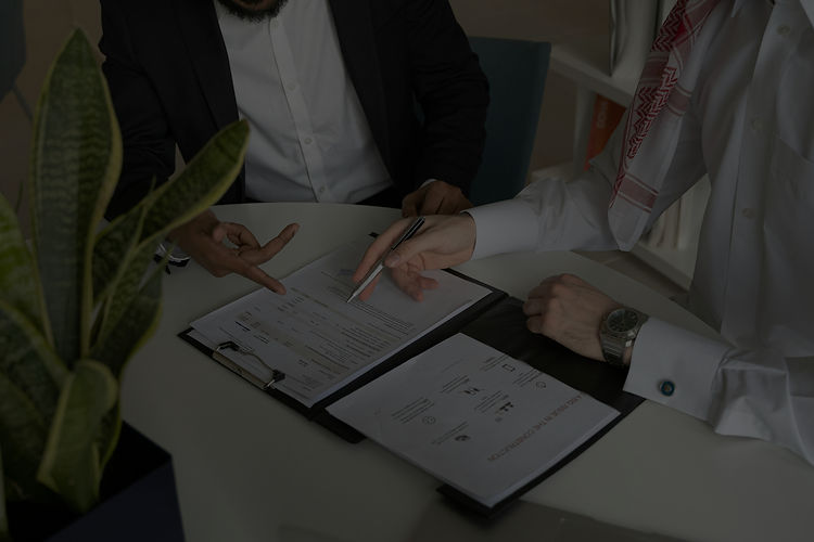 Two men sit at a table, reviewing documents and discussing their contents.