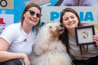 Tutoras sorrindo com cachorro peludo na 1ª Cãominhada Pet da Praia do Gravatá em Navegantes.