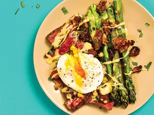 A plate of asparagus and steak with a soft boiled egg on top