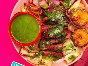 An overhead shot of steak with a salsa and grilled lemons.