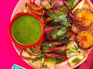 An overhead shot of steak with a salsa and grilled lemons.