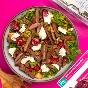 An overhead shot of a big bowl of steak and lettuce with beets and goat cheese