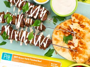 An overhead shot of kabobs and sauce with herbs on a cutting board.