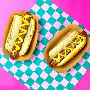 2 hot dogs on a green checked paper, with mustard.
