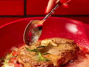 A spoon scooping butter on top of a ribeye steak.