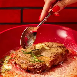 A spoon scooping butter on top of a ribeye steak.