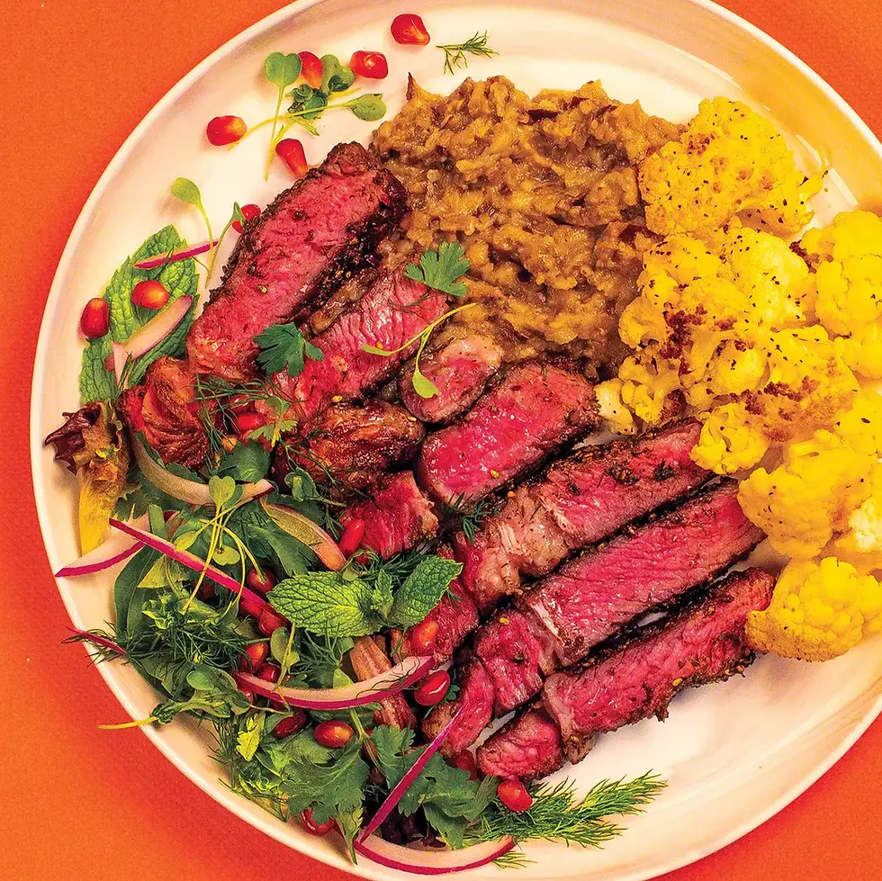 A sliced and spiced steak on a plate with salad and cauliflower.