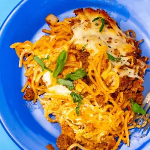 Cheesy spaghetti casserole with basil on a bright blue plate, close-up food shot with melted cheese and browned meat sauce.
