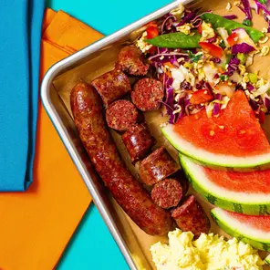An overhead view of hot links on a tray with coleslaw and watermelon.
