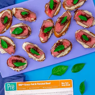 Overhead view of Italian-inspired Venetian cicchetti featuring grass-fed, pasture-raised New York strip steak crostini topped with creamy spread, sun-dried tomato tapenade, and fresh basil on toasted baguette slices, served as an elegant appetizer.