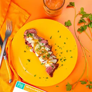 Overhead view of a Pre New York Strip steak on an orange plate with chives and blue cheese sauce.