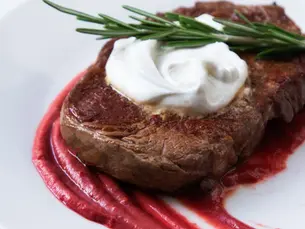 A ribeye steak on a bed of beet pureé and topped with whipped chévre