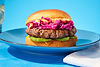 A burger with red onion, avocado and chili mayo