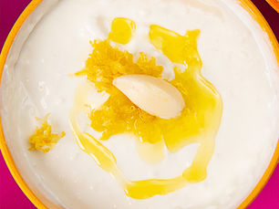 Overhead shot of a creamy white sauce and a drizzle of olive oil and a single garlic clove and lemon rind shavings in the center.