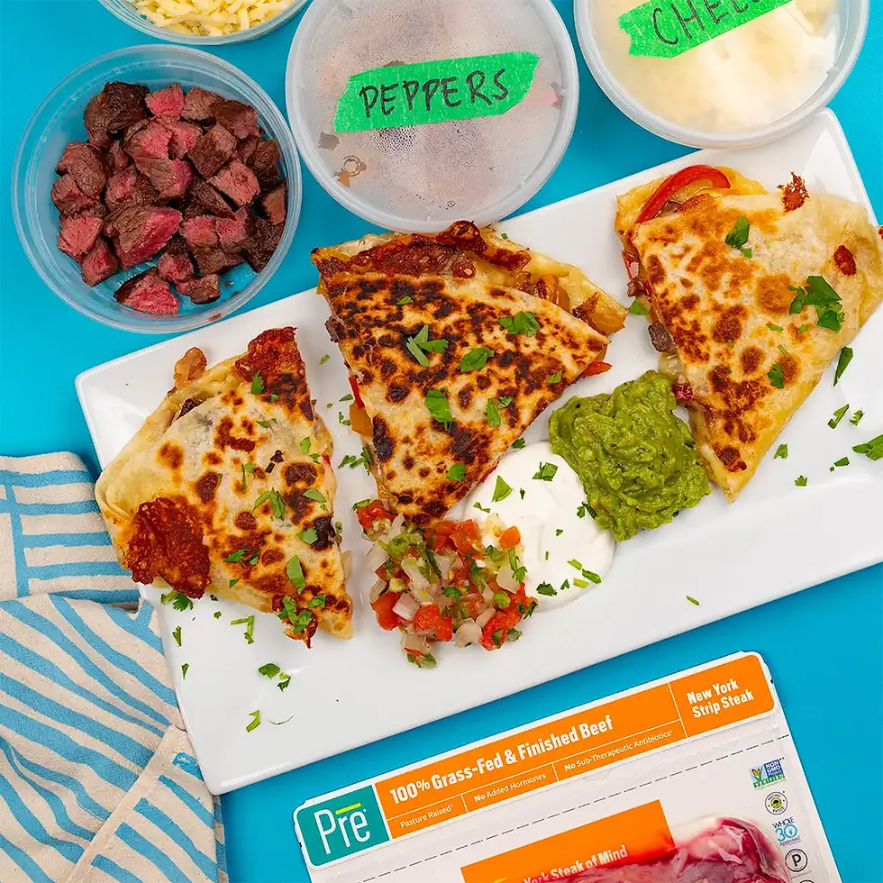 Overhead view of cheesy steak quesadilla wedges on a white plate with guacamole, sour cream, pico, and labeled peppers and cheese.