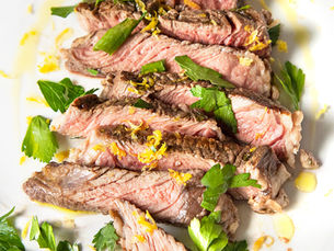 Sliced steak topped with green herbs and lemon zest
