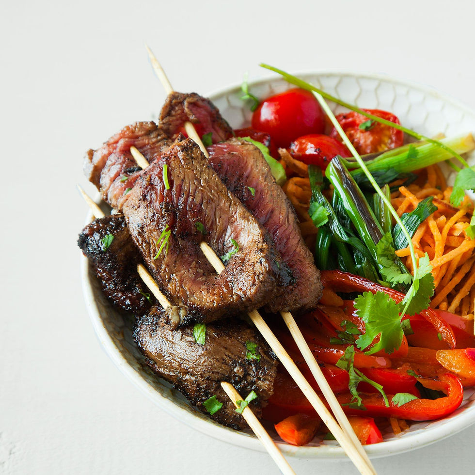 Jamaican jerk skewers on top of a bowl of sliced peppers and tomatoes.