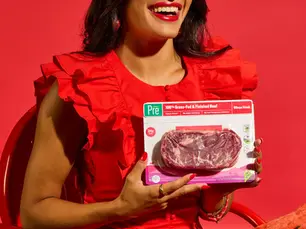 Woman laughing and smiling while holding a package of Pre® Ribeye steak.