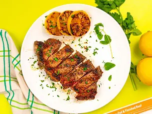 Sliced grilled beef and charred citrus on a white plate, with herbs, lemons, and a Pre 100% Grass-Fed & Finished Beef package on yellow.