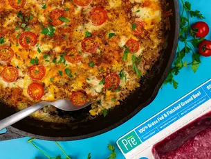 An overhead shot of a skillet full of macaroni and cheese with juicy beef, and a package of Pre® ground beef nearby.