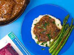 An overhead shot of salisbury steak on top of mashed potatoes with asparagus and a package of Pre Ground Beef.