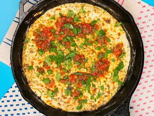 A big skillet full of cheese dip and topped with green onion.