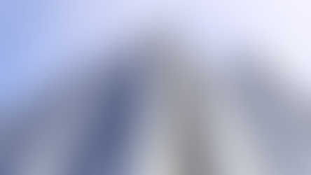 Curved glass office building reflecting a clear blue sky, surrounded by other skyscrapers and trees with yellow leaves on a sunny day. Urban setting.