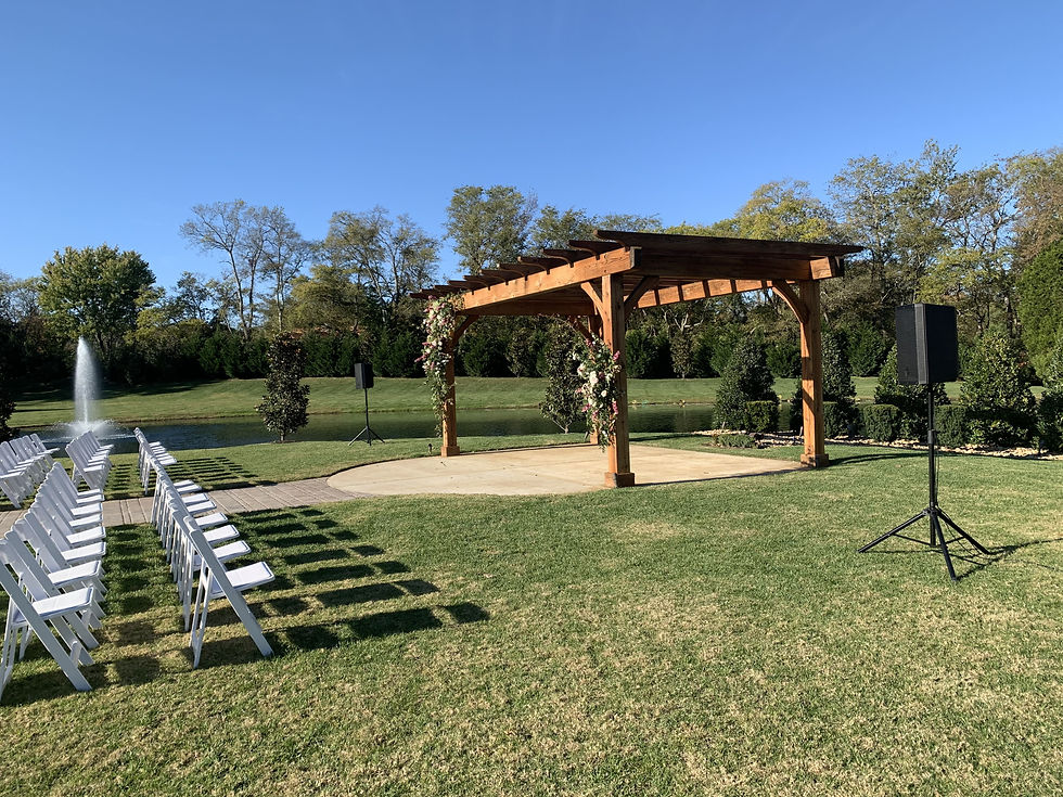 Outdoor wedding venue with a wooden pergola and fountain, with chairs arranged for a ceremony.