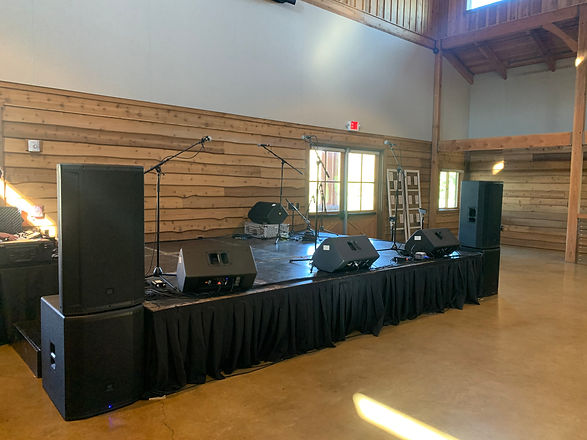 Three-way speakers on top of JBL subwoofers at a stage for a band performance during a wedding reception.