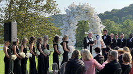 Bride and groom exchanging vows under a floral arch during an outdoor wedding ceremony.