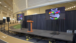 AV stage setup on an indoor track with two TVs showing test patterns and a podium at center