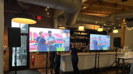 Indoor event setup with screens displaying sports highlights in a venue with industrial decor.