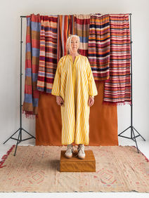portrait femme maghrébine avec un caftan rayé jaune, et des foutas marocaines en fond. portrait orientaliste revisité avec des baskets addidas.