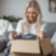 smiling blonde girl sitting on a couch pulling a t-shirt out of a box.jpg
