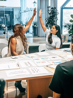 Two sitting business women high fiving at a desk