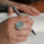 Blue and orange leaf aluminium silver rivet ring on a white woman with pen and notebook
